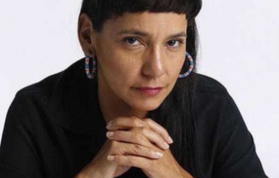 Indigenous choreographer Rosy Simas with hands clasped, wearing a black shirt and colorful beaded hoop earrings
