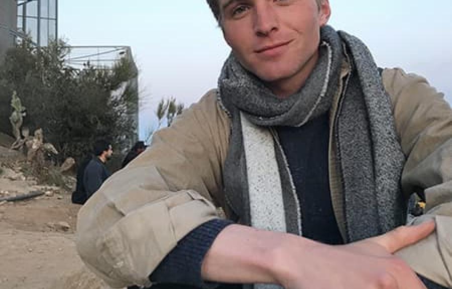 Nathan Revor wearing a coat and scarf with desert and sunset visible in background