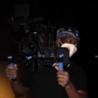 Photo of Joshua Akinwumi on set holding a camera