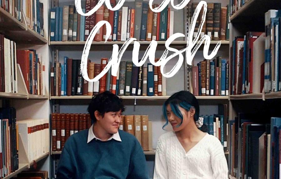 Two people sitting on the floor side by side against library stacks looking at each other. "A Musical Short Film: Class Crush"