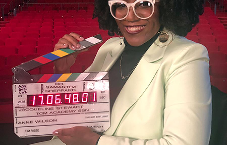 Photo of Dr. Samantha Sheppard holding a clapper board inside a large theatre
