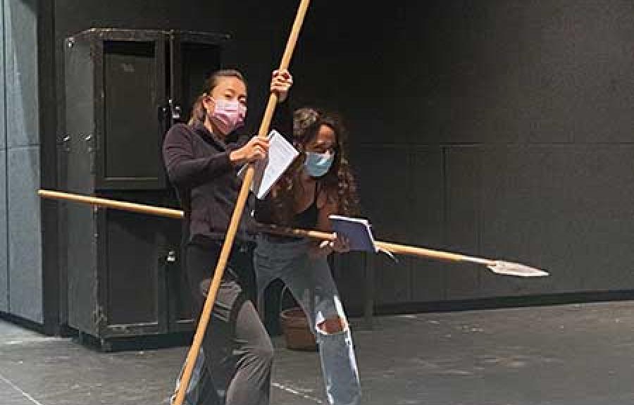 Two actresses holding spears on stage for a Seven Homeless Mammoths Wander New England rehearsal