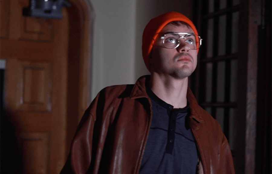 Man in glasses, jacket, and knit hat standing inside a darkened building