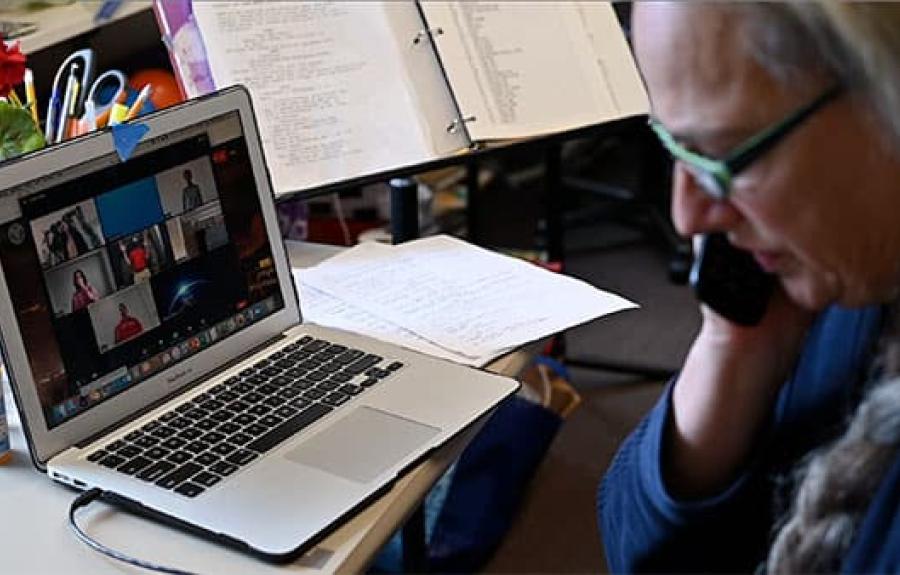 A professor on her cellphone with a zoom class visible on laptop in front of her