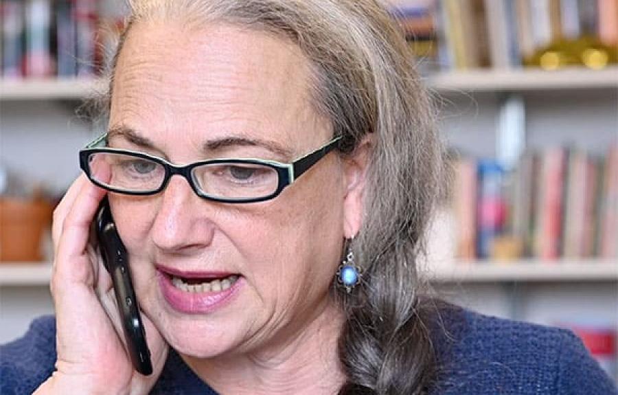 A professor on her cell phone in an office with bookshelves lining the wall behind her