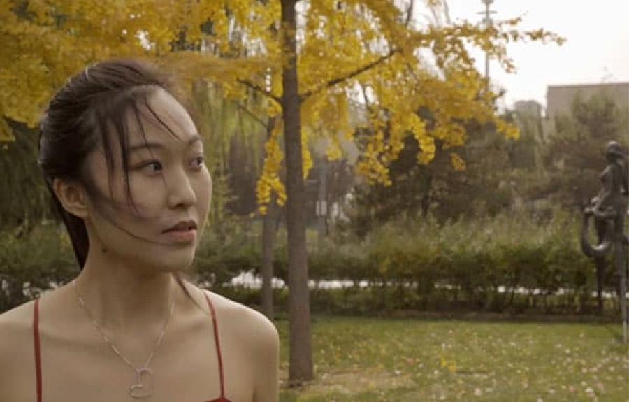 Young woman looking off to the side with trees, grass, and buildings in the background