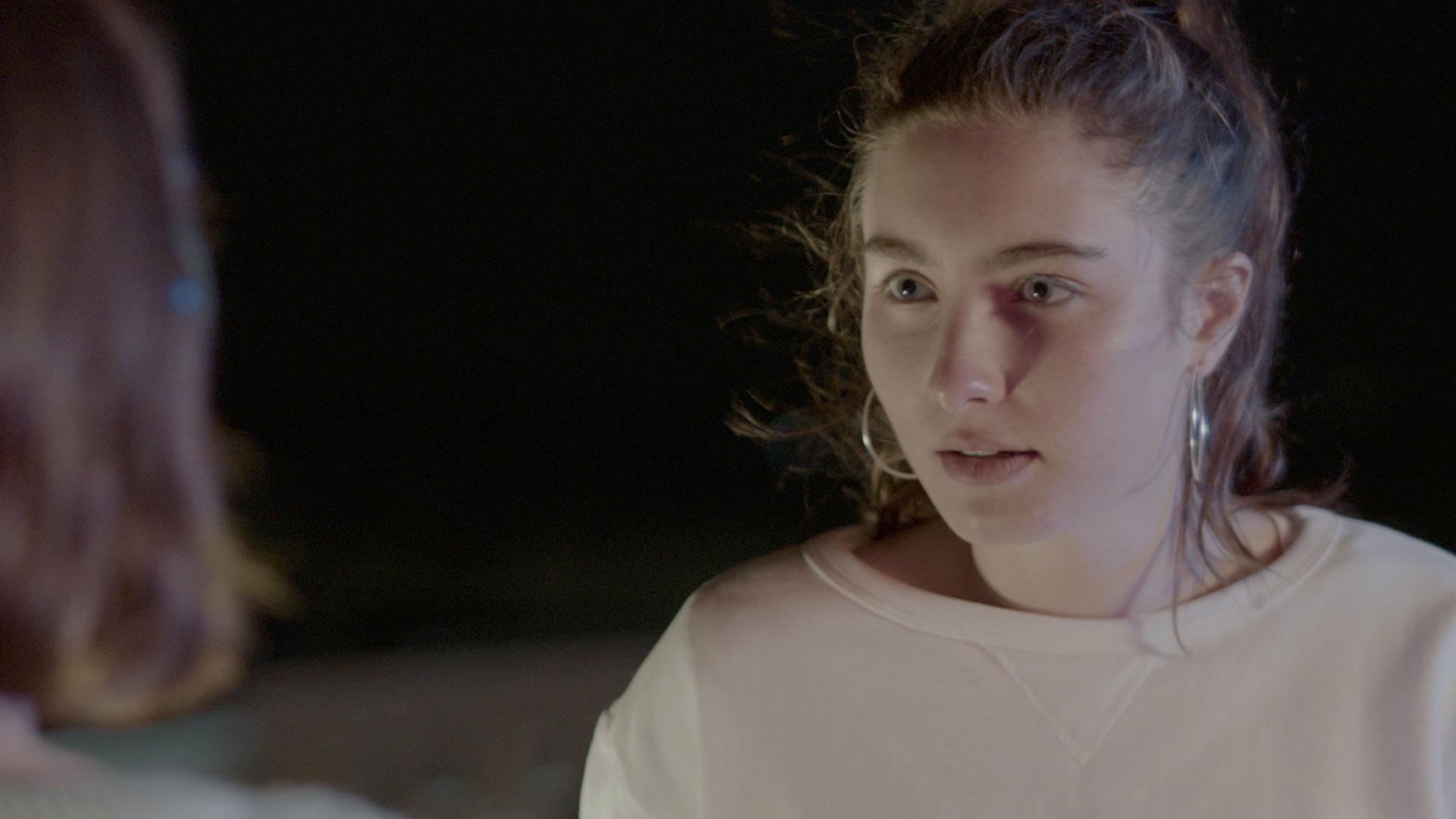 A young woman looks at another person outdoors at night.