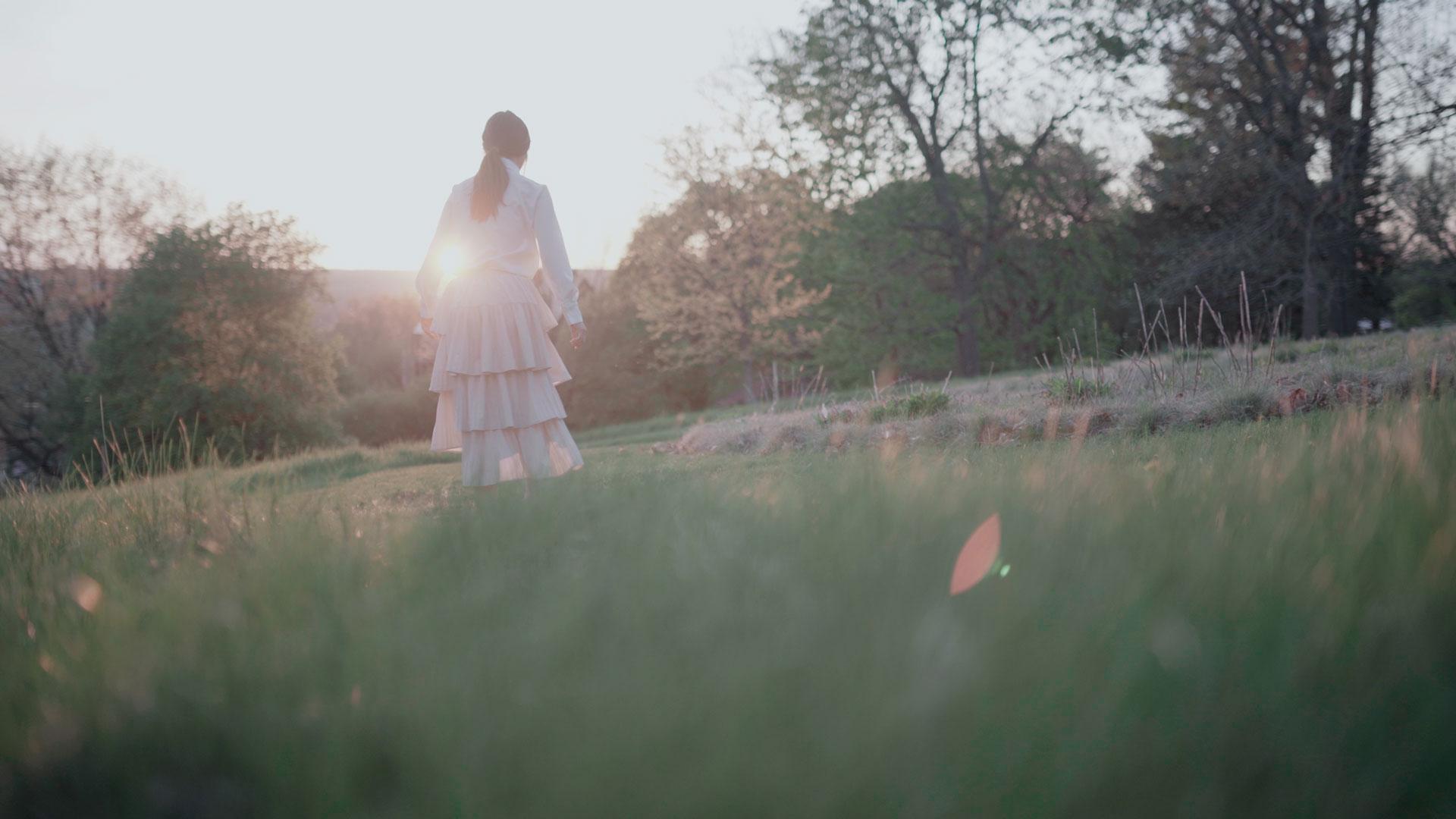 A woman walks in a field at sunset.