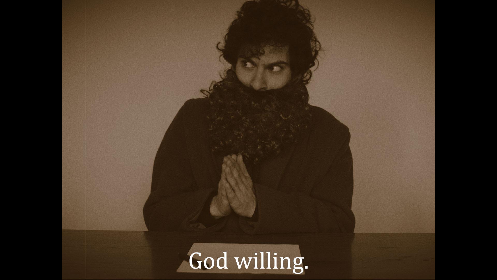 A young man wearing a false bear is sitting at a table with his hands in prayer position.