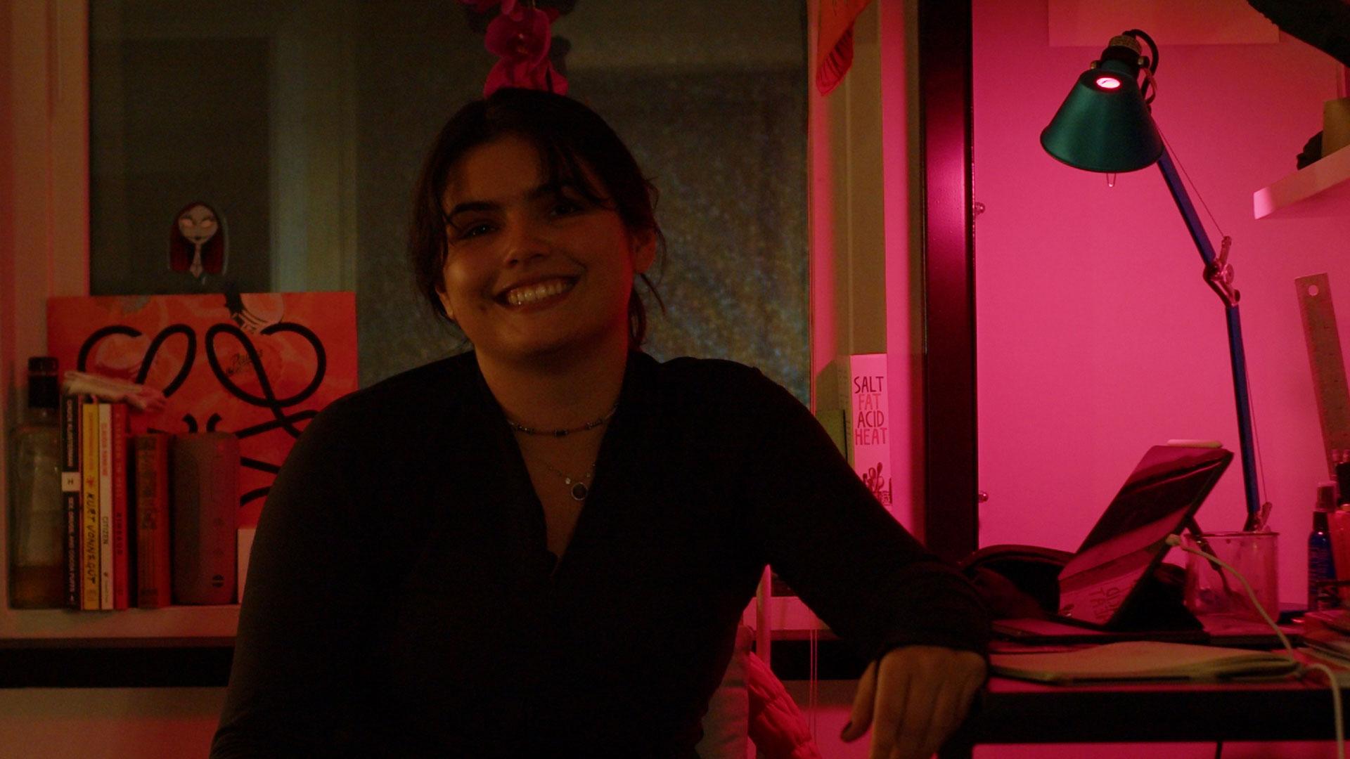 A young woman sitting in a room smiling towards the camera.