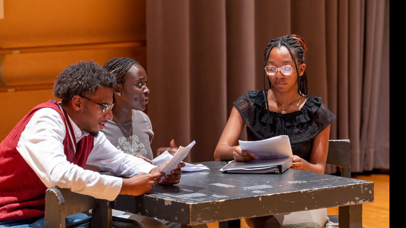 Three students sit around a table on stage reading from scripts in the Class of ’56 Dance Studio Theatre.