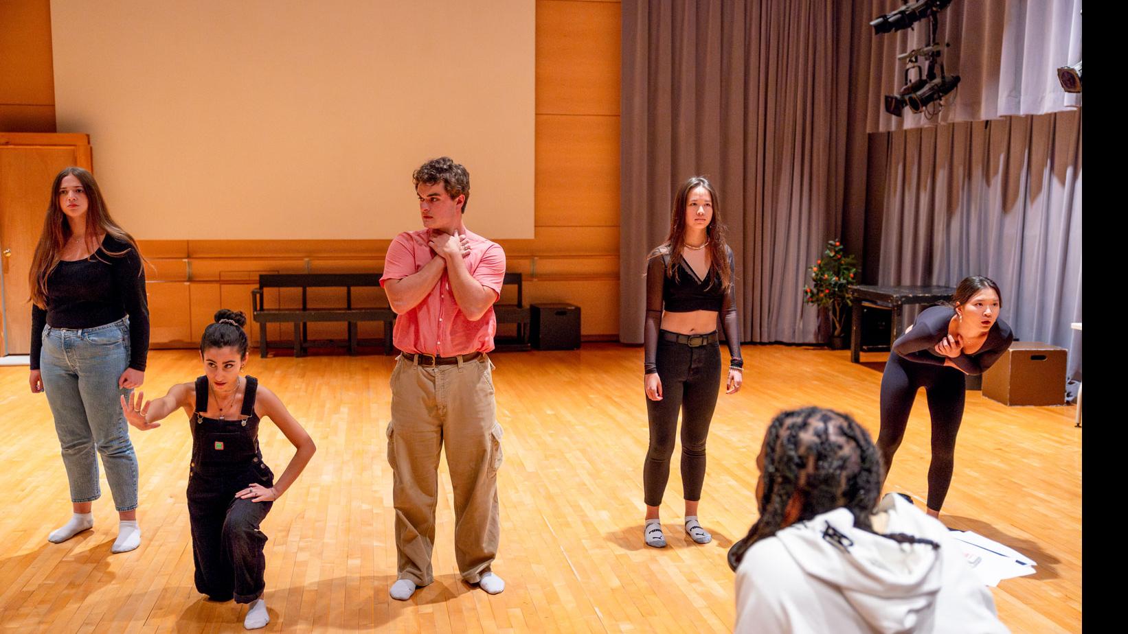 Five students stand on stage in movement poses, while Daveed Diggs looks on in the Class of ’56 Dance Studio Theatre.