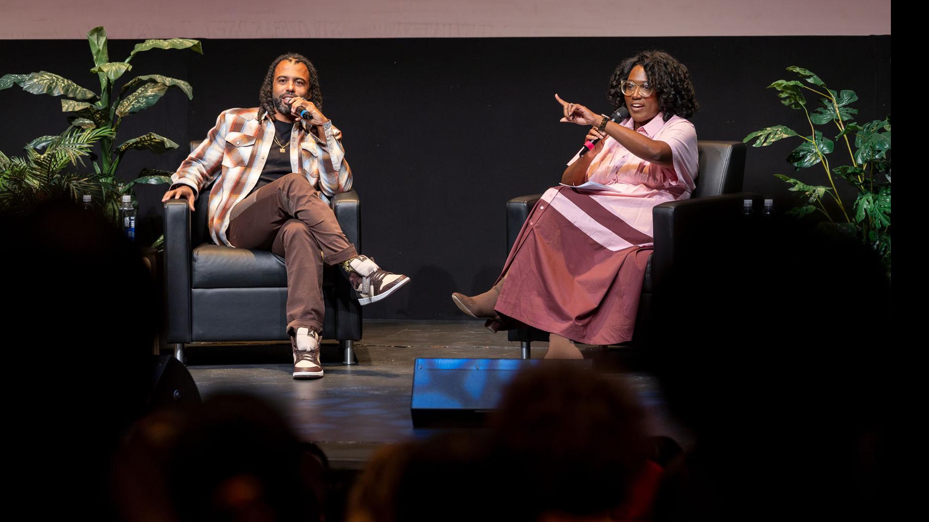 Daveed Diggs sits and speaks into a microphone on stage and PMA Department Chair Samantha Noelle Sheppard points towards the audience in the Kiplinger Theatre.