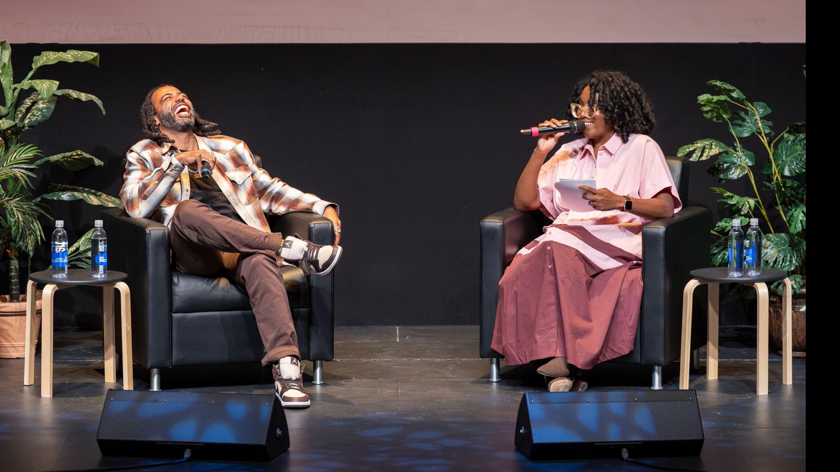 Daveed Diggs laughs and PMA Department Chair Samantha Noelle Sheppard speaks into a microphone on stage in the Kiplinger Theatre.