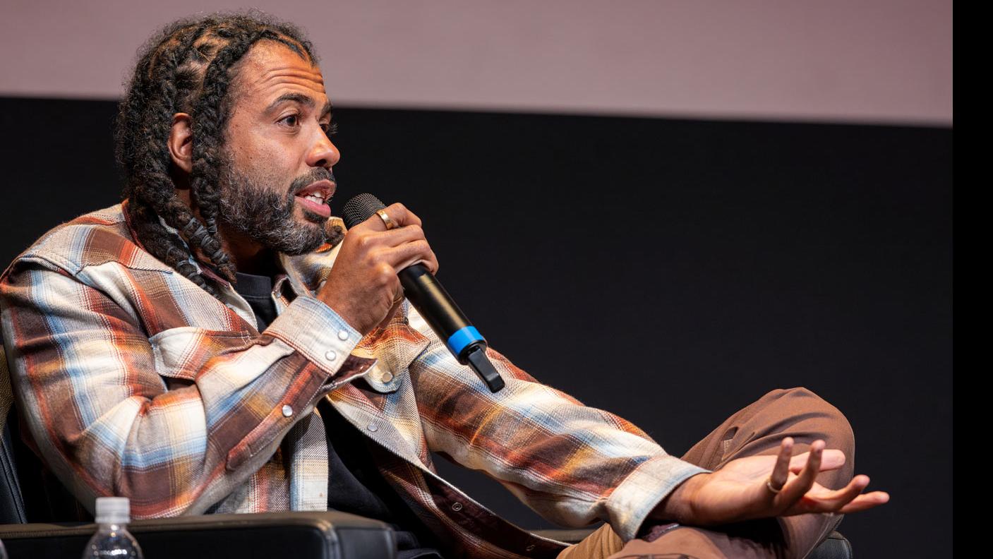 Daveed Diggs sits and speaks into a microphone on stage in the Kiplinger Theatre.