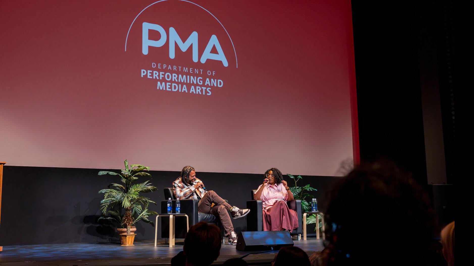 Daveed Diggs and PMA Department Chair Samantha Noelle Sheppard sit on stage and speak into microphones in the Kiplinger Theatre, with a large screen showing the PMA logo.