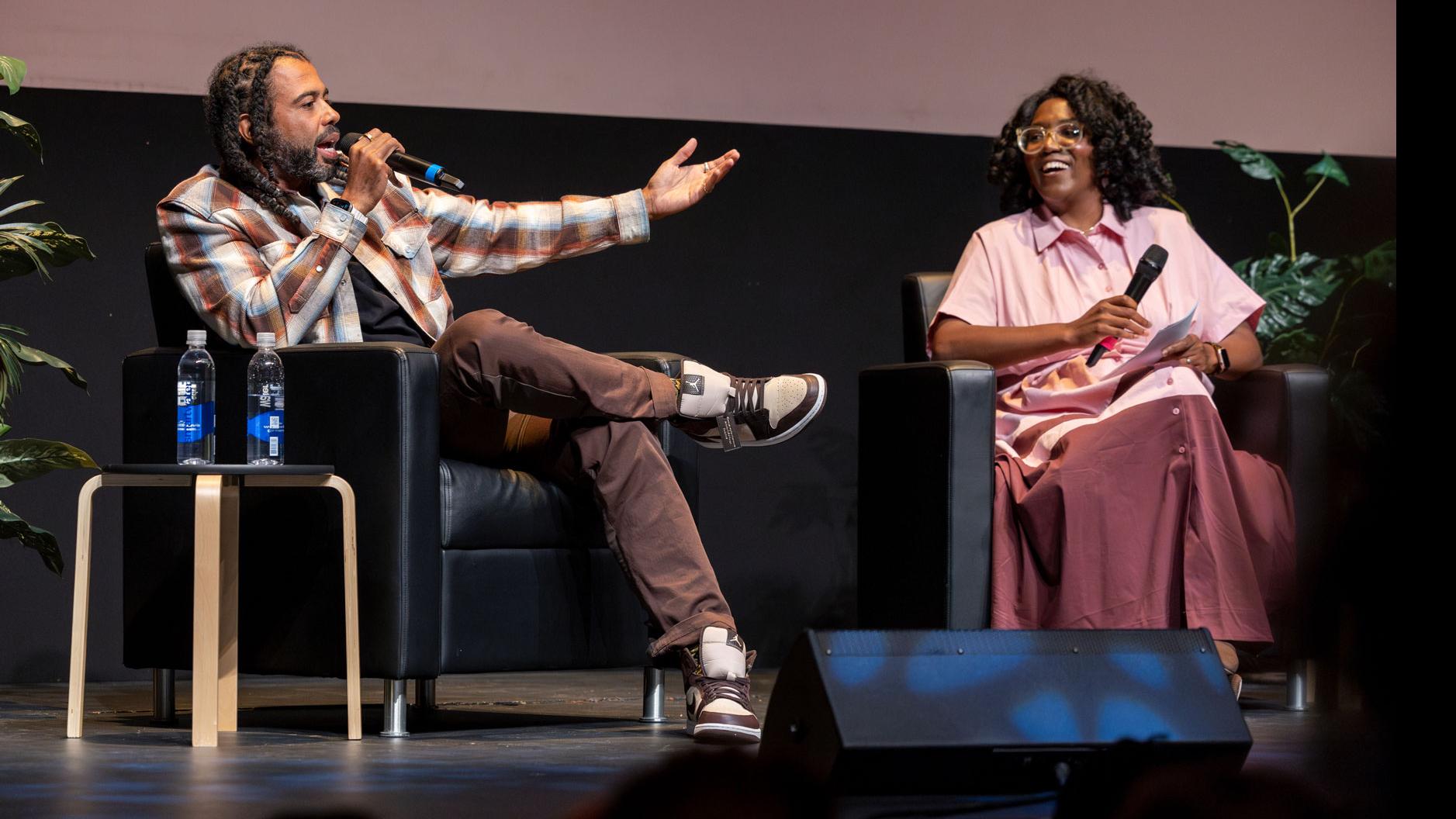 Daveed Diggs speaks into a microphone and PMA Department Chair Samantha Noelle Sheppard laughs on stage in the Kiplinger Theatre.