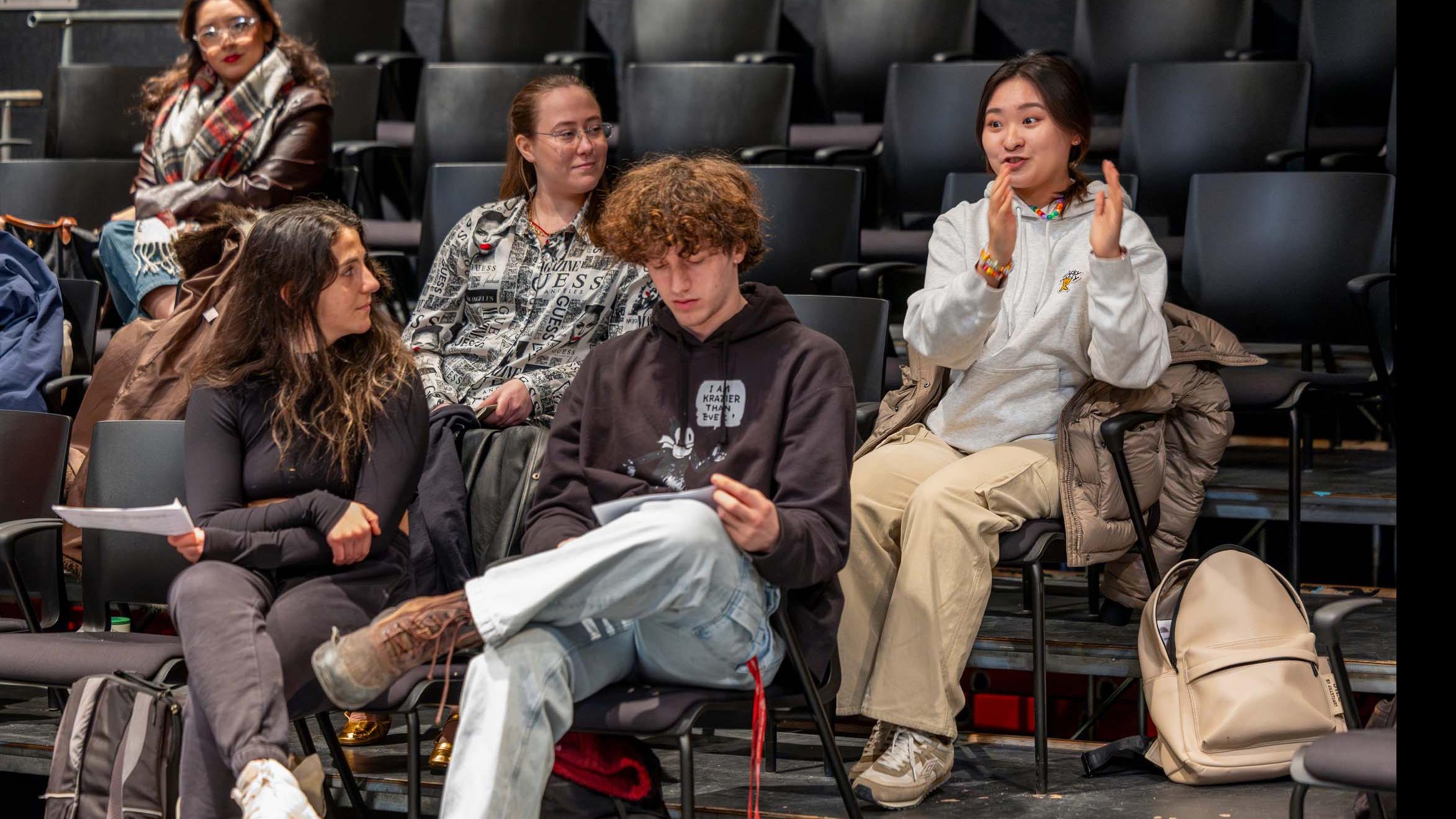 A student speaks from the audience in the Black Box Theatre, while four other students look on.