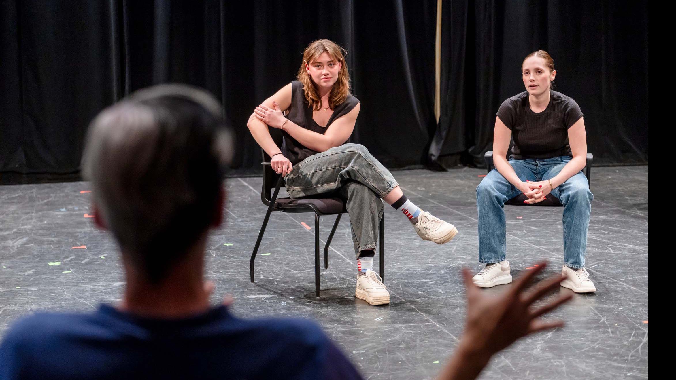 In the foreground, John Cameron Mitchell faces away towards two students seated and on stage in the Black Box Theatre looking back at him. Photo credit: Simon Wheeler