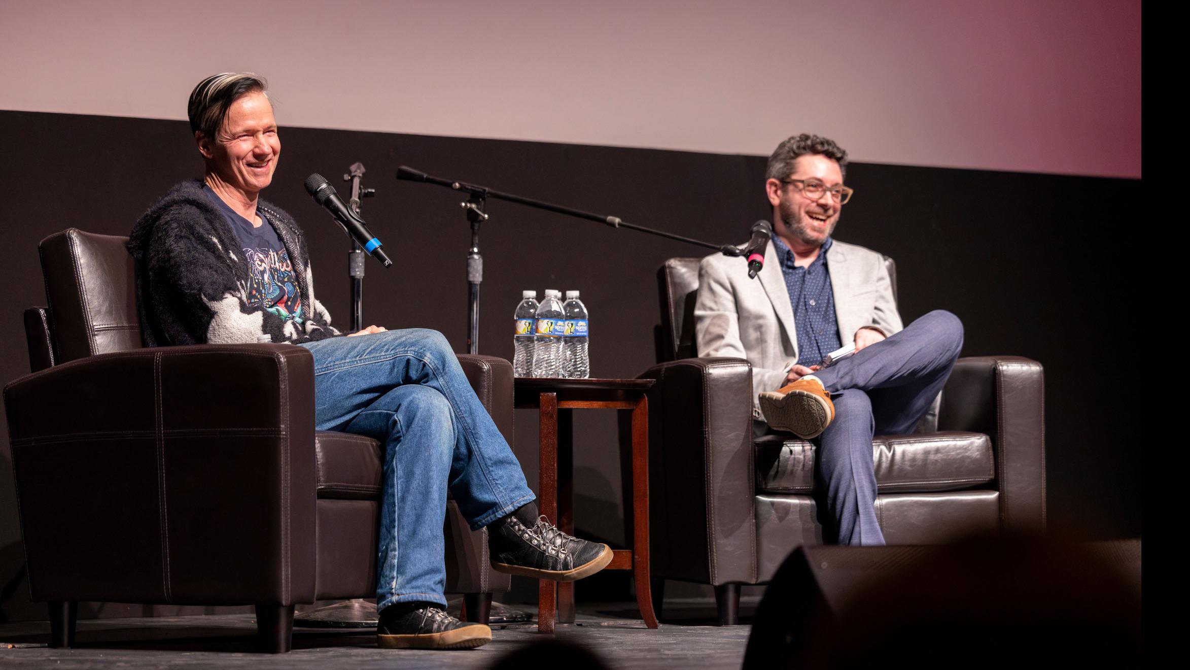 John Cameron Mitchell and PMA faculty member Nick Salvato smile and look into the audience on stage in the Kiplinger Theatre. Photo credit: Simon Wheeler