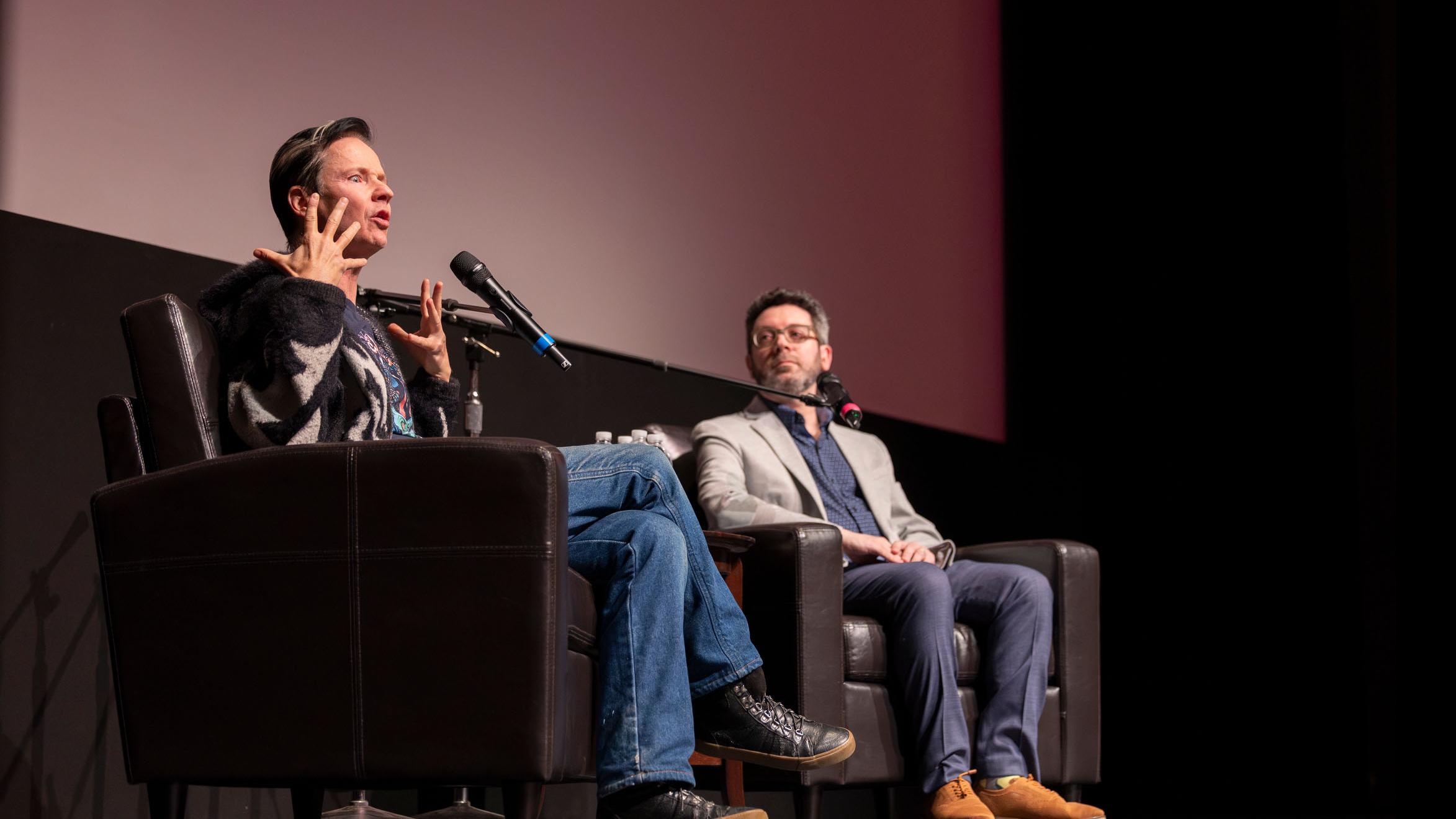 John Cameron Mitchell gestures and speaks while PMA faculty member Nick Salvato looks over, on stage in the Kiplinger Theatre. Photo credit: Simon Wheeler