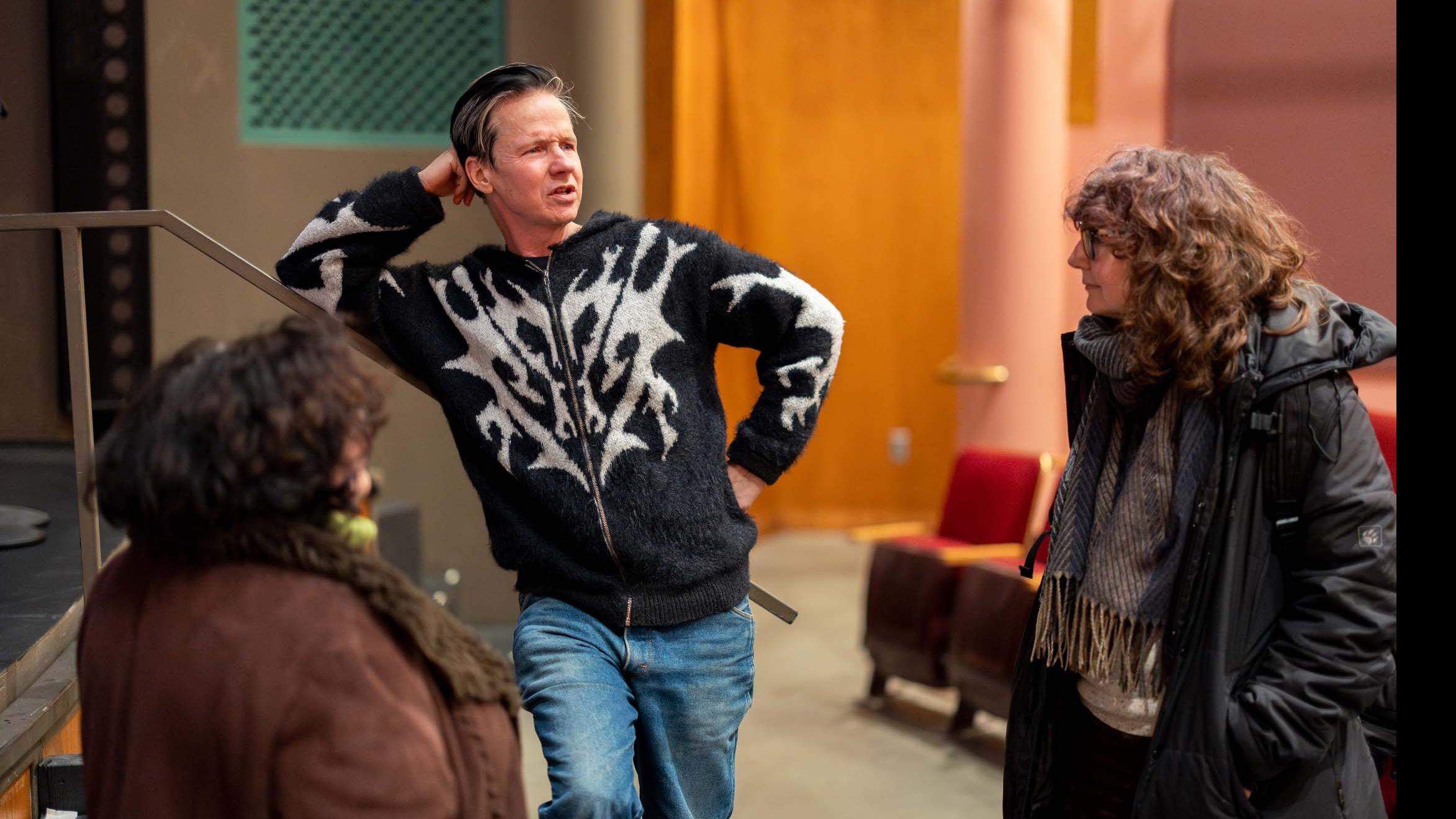 John Cameron Mitchell leans on a banister and speaks with two people in the orchestra section of the Kiplinger Theatre. Photo credit: Simon Wheeler