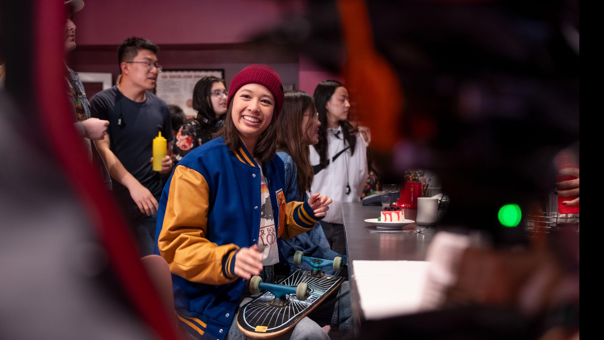 A student actor smiles at the camera while student crew members stand in the background on the set of the PMA Studios short film Milkshake Kiss. Photo credit: Simon Wheeler