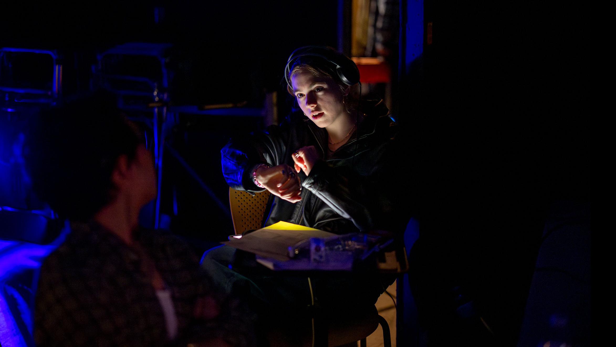 Two student crew members hold scripts and talk in dim lighting on the set of the PMA Studios short film Milkshake Kiss. Photo credit: Simon Wheeler