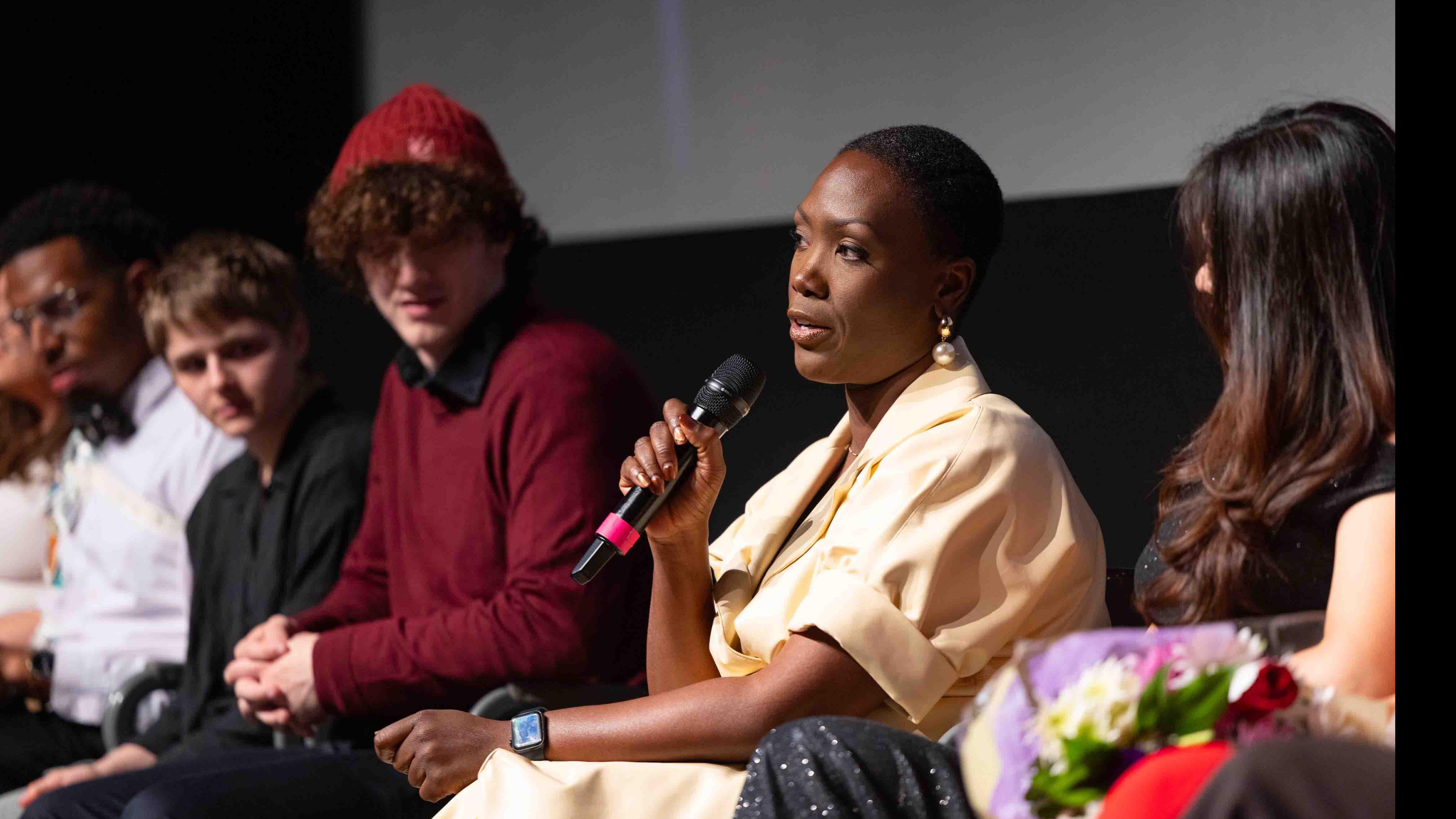 PMA Visiting Lecturer Carolyn Michelle Smith speaks into a microphone surrounded by student cast and crew members of the PMA Studios short film Milkshake Kiss on stage in the Kiplinger Theatre. Photo credit: Chris Kitchen