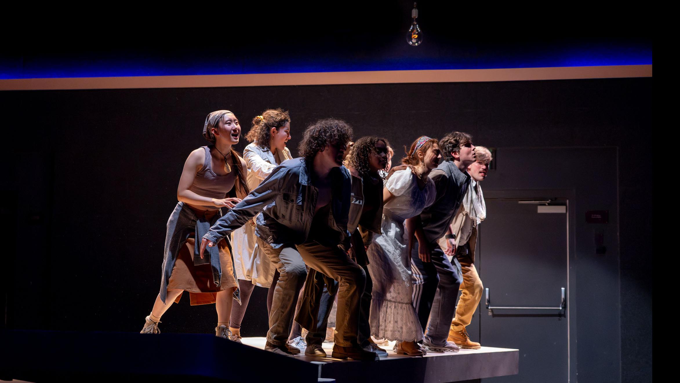An ensemble of performers group together and lean forward in movement poses during a performance of I Want a Country in the Flex Theatre, Schwartz Center for the Performing Arts.
