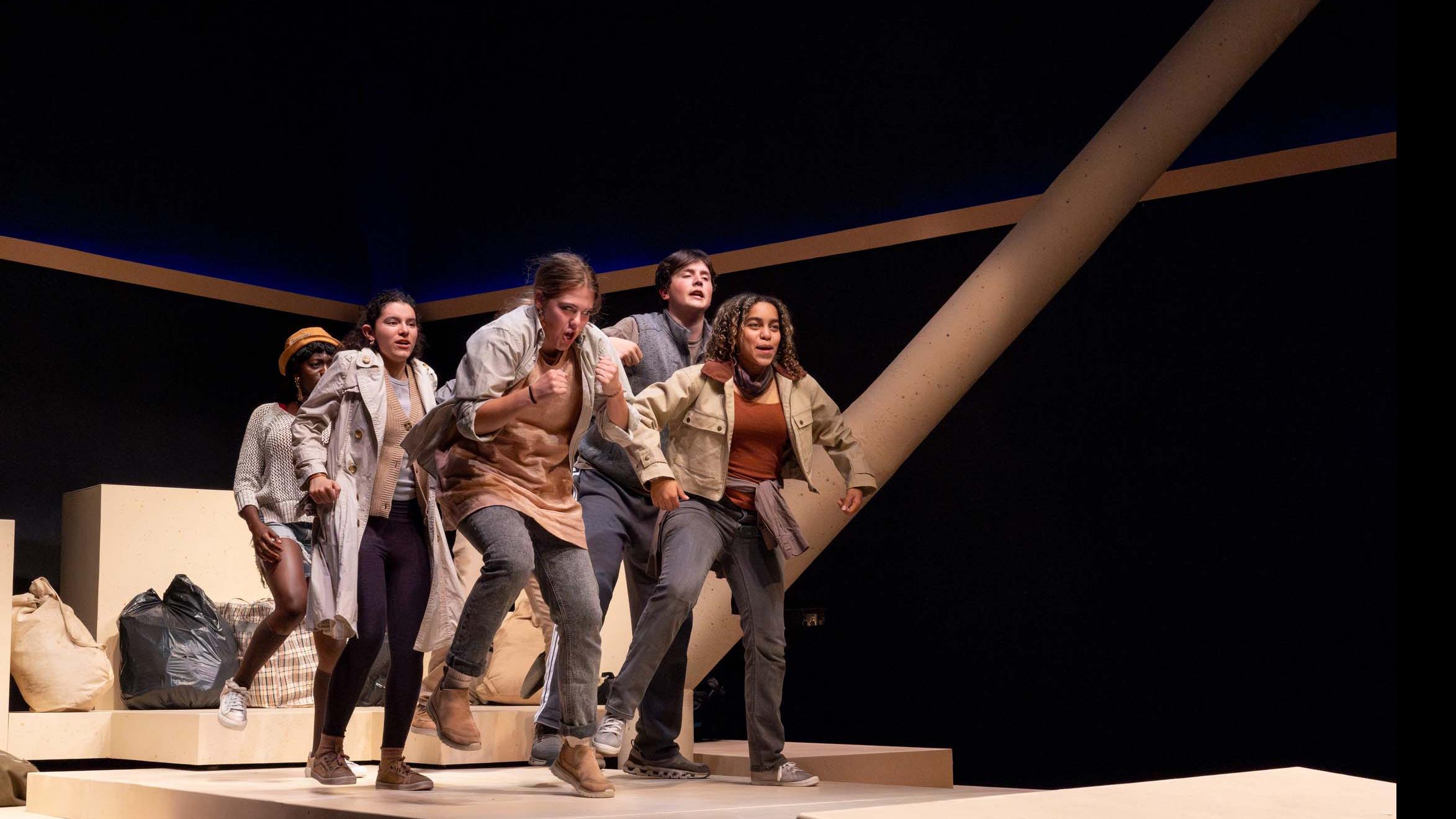 An ensemble of performers group together and hop in movement poses during a performance of I Want a Country in the Flex Theatre, Schwartz Center for the Performing Arts.
