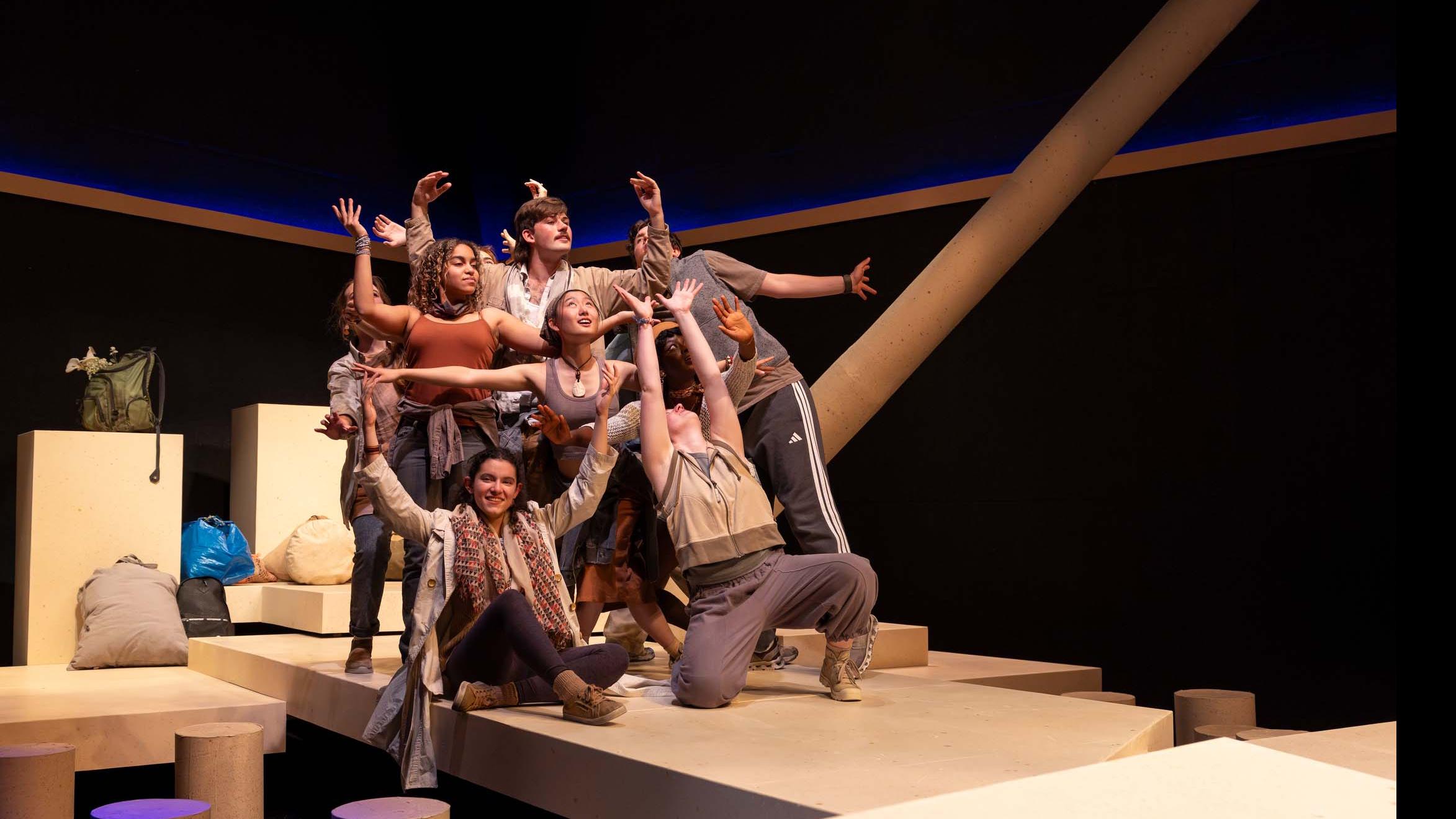 An ensemble of performers group together sitting and standing with arms raised during a performance of I Want a Country in the Flex Theatre, Schwartz Center for the Performing Arts.