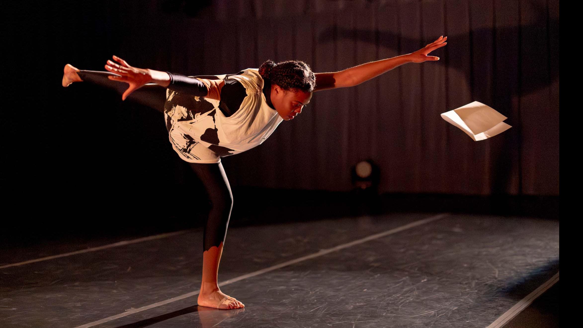 Amirah Ricks stands on one leg in a movement pose during Share In / Share Out in the Class of ’56 Dance Studio Theatre, Schwartz Center.