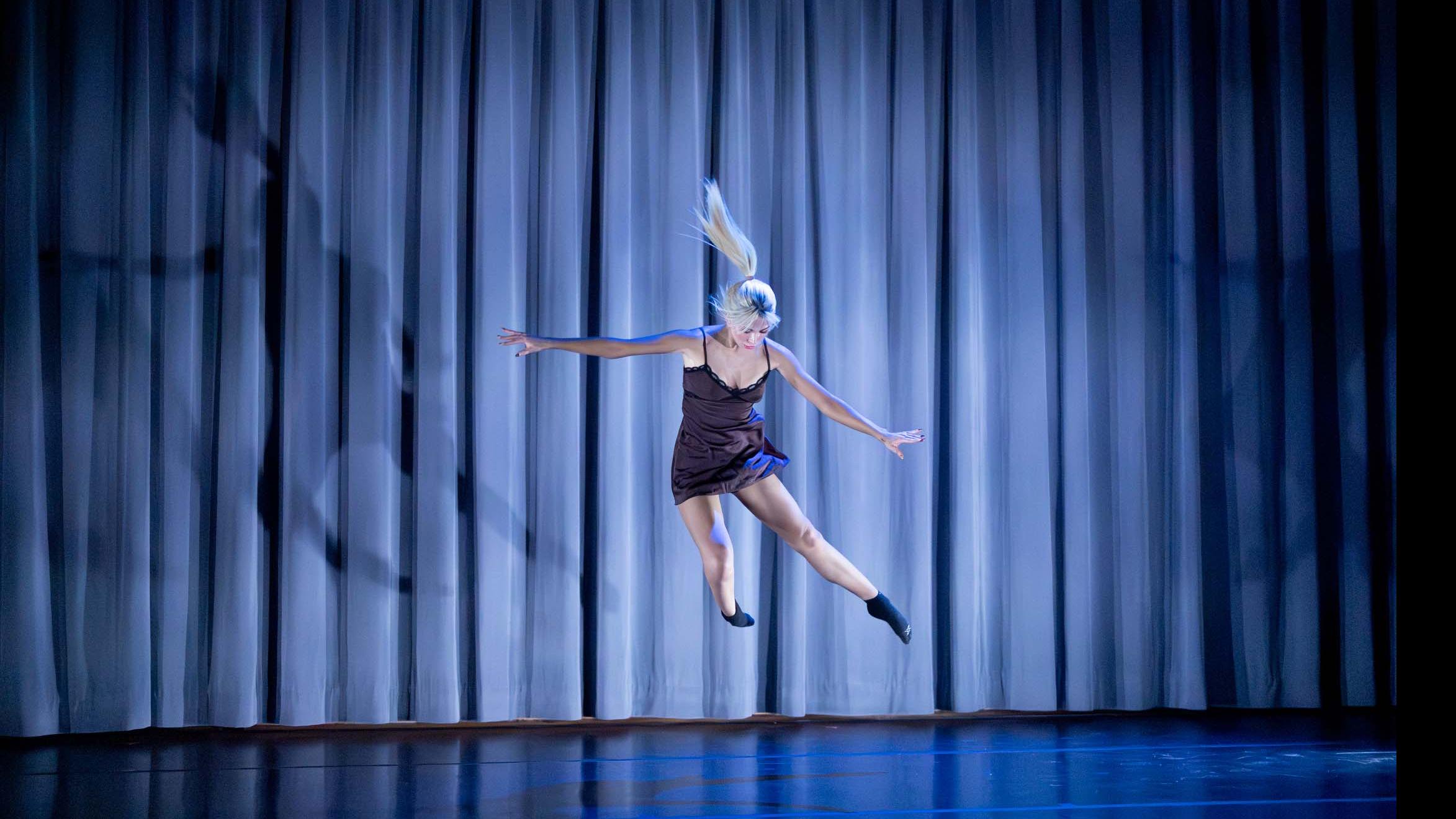 Jillian Vondell jumps sideways in a movement pose during Share In / Share Out in the Class of ’56 Dance Studio Theatre, Schwartz Center.