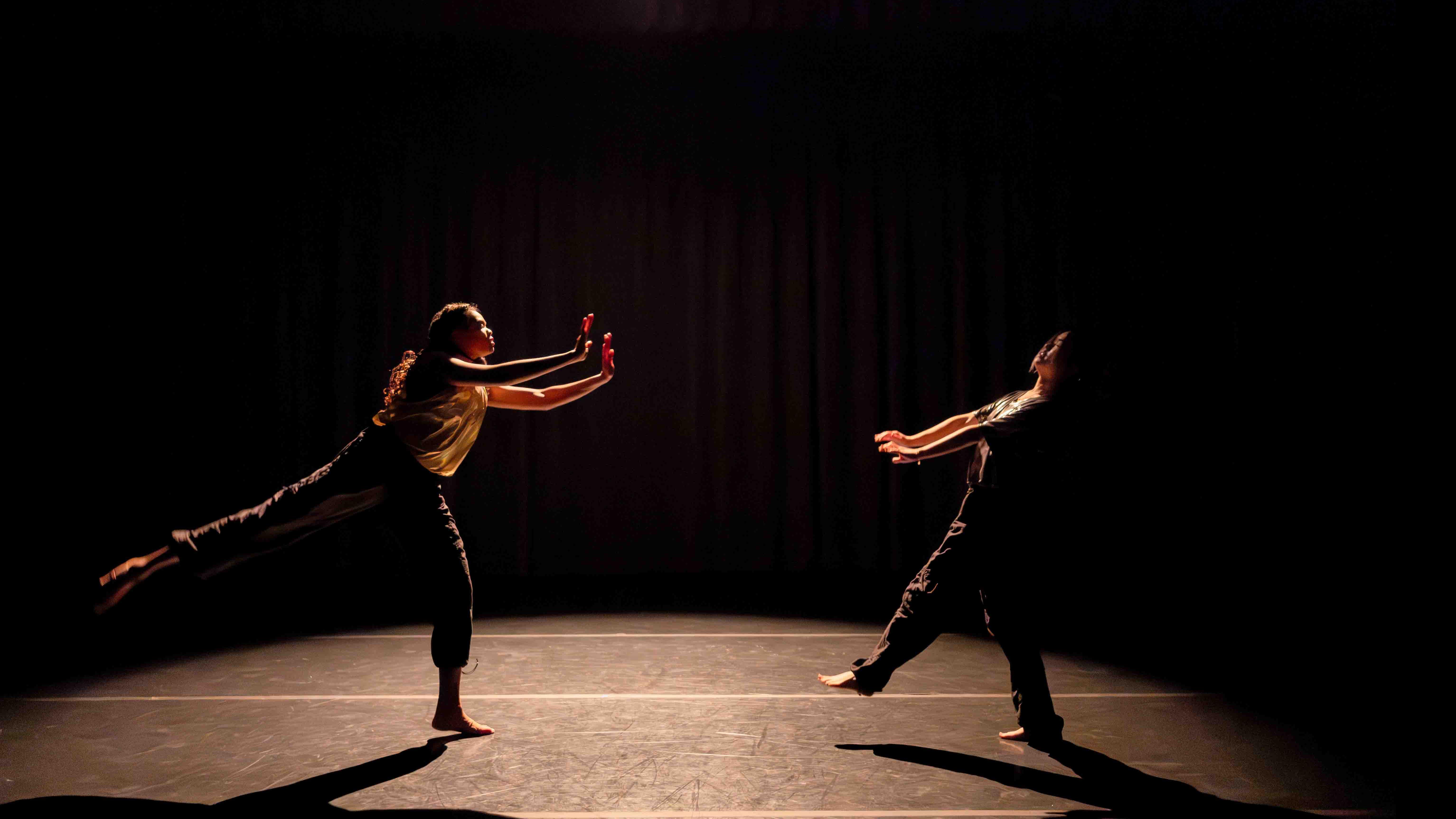On left, Amirah Ricks, on right Agnes Sun reach towards each other in movement poses during Share In / Share Out in the Class of ’56 Dance Studio Theatre, Schwartz Center.