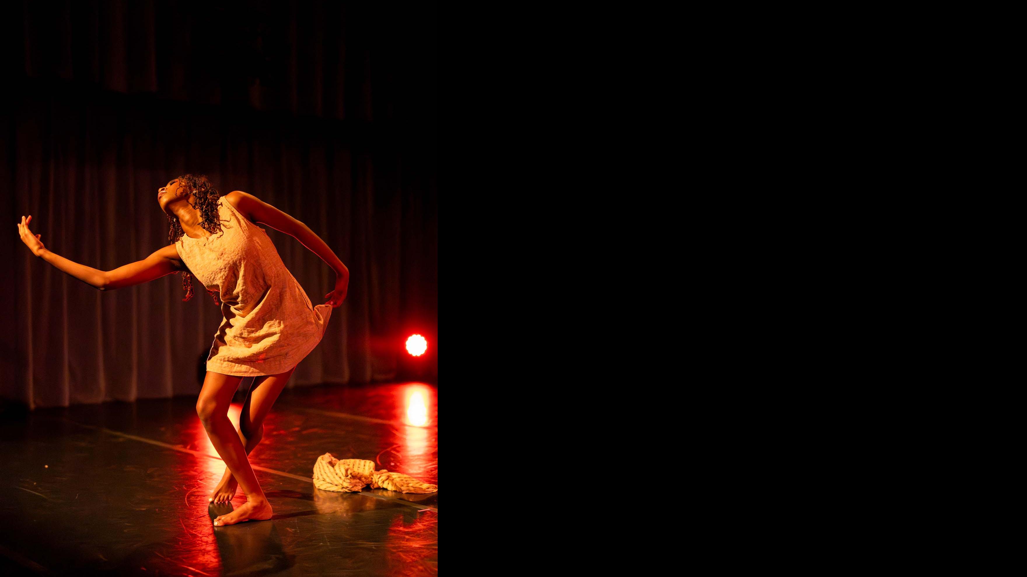 Kaelyn J. Stewart reaches forward in a movement pose during Share In / Share Out in the Class of ’56 Dance Studio Theatre, Schwartz Center.