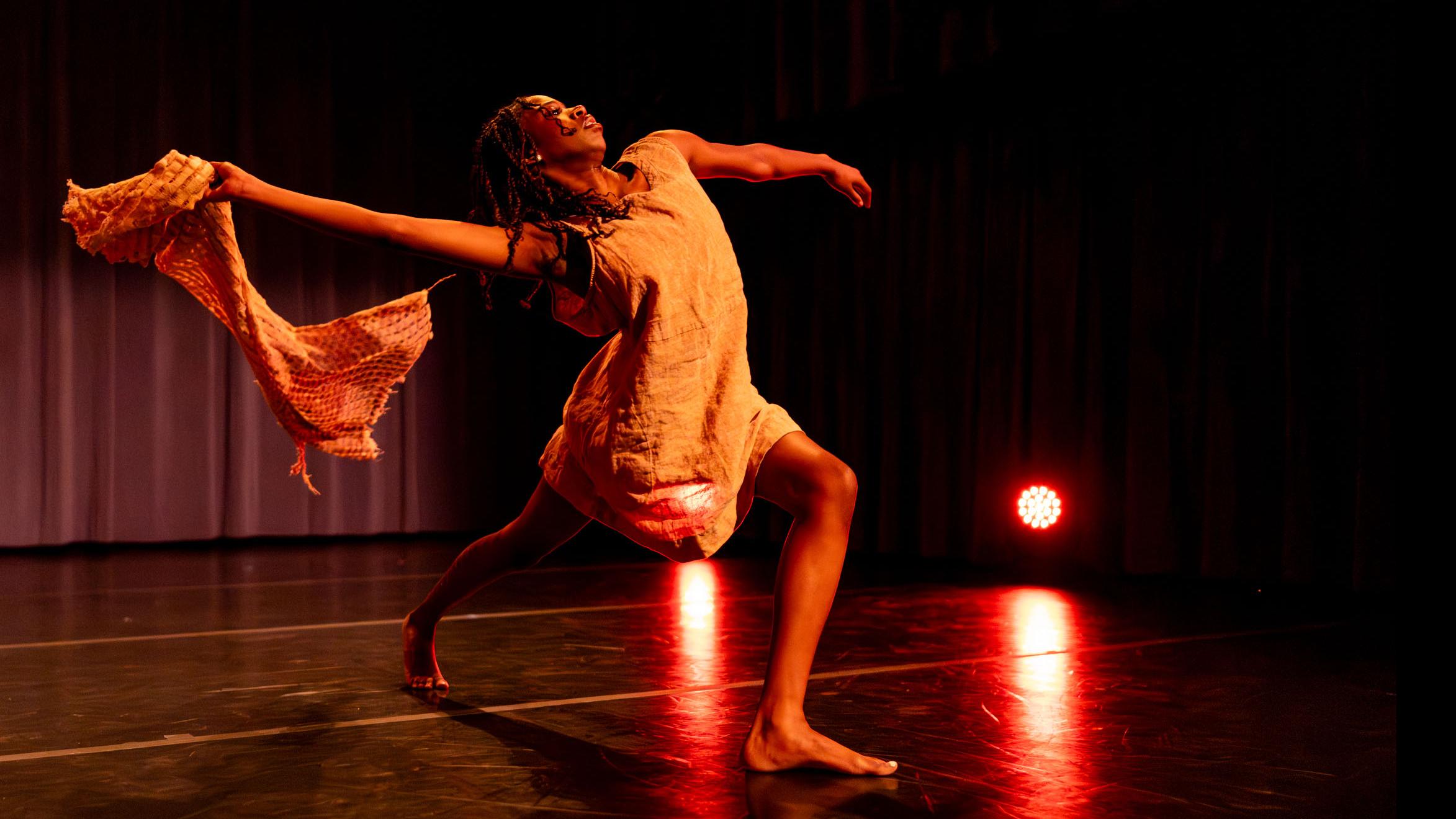 Kaelyn J. Stewart strides forward in a movement pose during Share In / Share Out in the Class of ’56 Dance Studio Theatre, Schwartz Center.