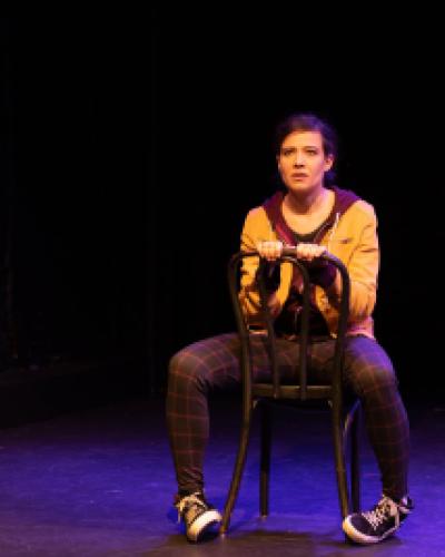 Molly Carden sitting on a chair backwards on stage looking into the distance