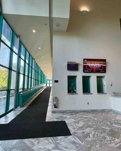 Schwartz Center for the Performing Arts main floor lobby, angling up the ramp towards the front door on the left, with three box office windows on the right.