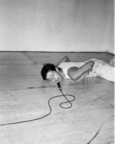 Roya Carreras Fereshtehnejad on the ground in a movement pose facing a microphone and cord that are coiled on the ground.