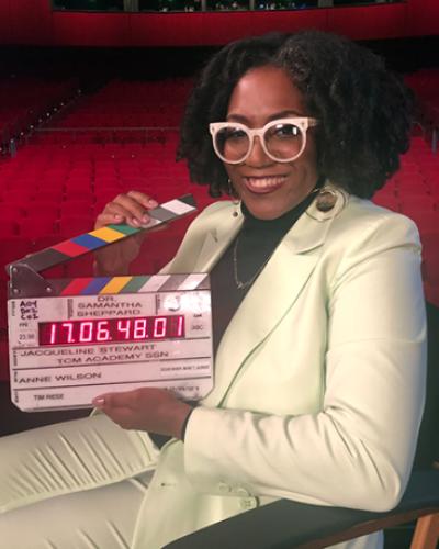 Photo of Dr. Samantha Sheppard holding a clapper board inside a large theatre